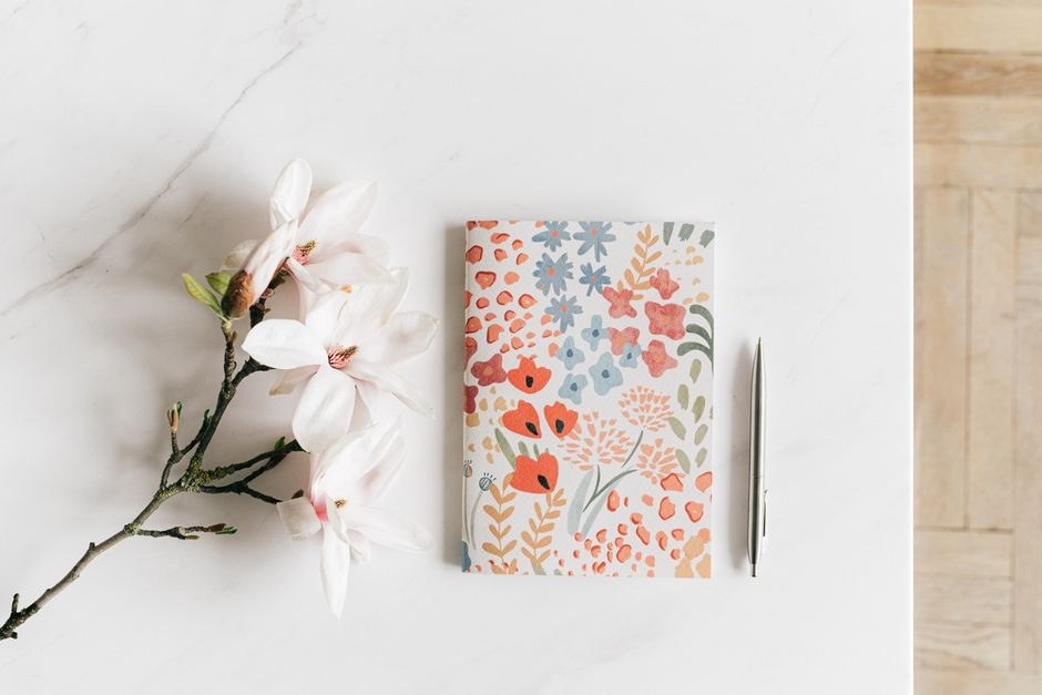 A patterned notebook, pen, and flowers on a light desk.